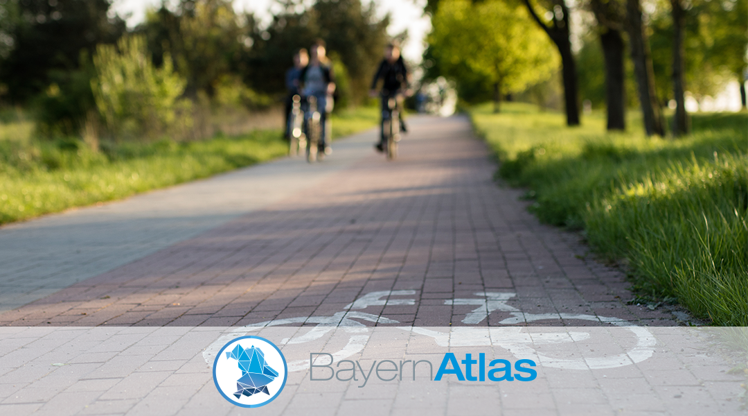 Thema Radwege im BayernAtlas Radweg in einer Naturlandschaft, vorne ist ein Radsymbol zu sehen, unten im Bild ist das Logo des BayernAtlas.